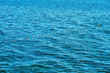 Sürekli mavi deniz suyu yüzeyi. Küçük bir dalga ve küçük şamandıralar eskrim ve güvenlik için sıraya dizildi.