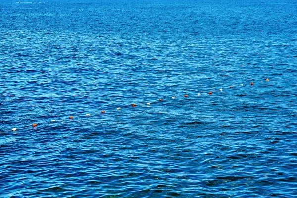 连续的蓝色海水表面 有一个小波浪和连续的小浮标 以确保栅栏和安全 — 图库照片