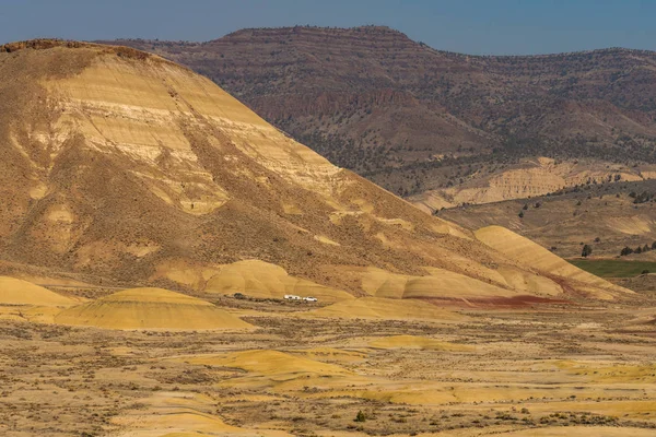 Samochody w oddali przejeżdżając przez pustynny, falujący i kolorowy krajobraz Painted Hills — Zdjęcie stockowe