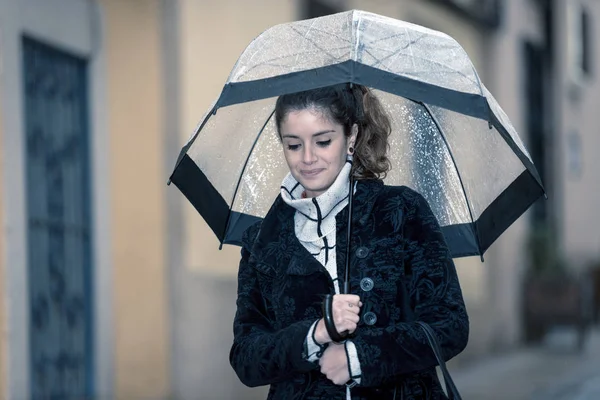 Joven morena camina por las calles de Cáceres con un paraguas transparente en un día lluvioso — Foto de Stock