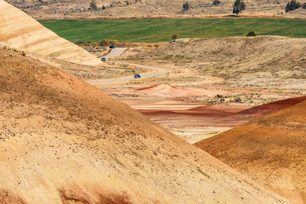 Coches en la distancia cruzando el desierto, ondulado y colorido paisaje de Painted Hills —  Fotos de Stock