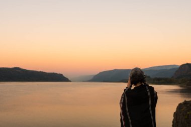 Pançolu genç bir kadın, Oregon, Columbia Nehri 'ndeki Corbett gözcüsünün günbatımının fotoğraflarını çekiyor.