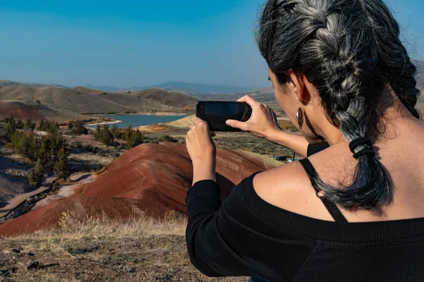 Egy fiatal nő sötét hajjal és ősz hajjal készít egy fényképet az okostelefonjával a Painted Hill víztározóból. — Stock Fotó