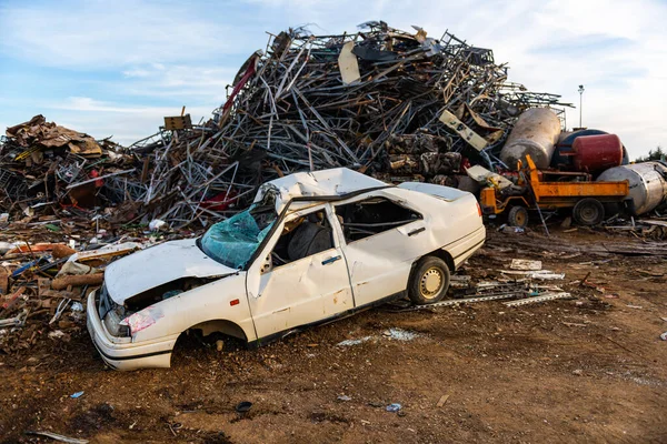 Broken and abandoned car next to a mountain of metal pieces in a junkyard