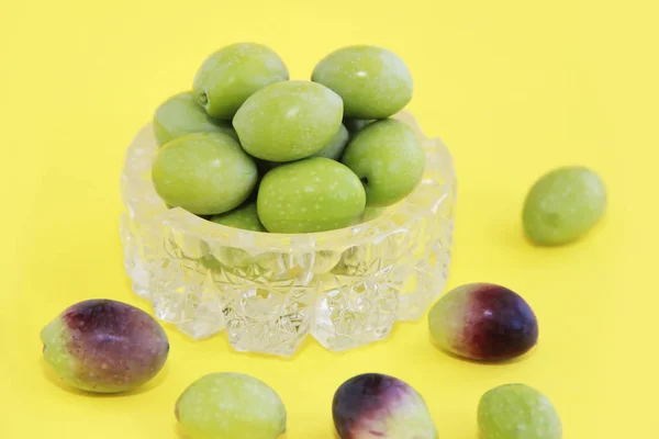 Natürliche frische runde grüne und braune Oliven in einem dekorativen Glasteller auf gelbem Hintergrund — Stockfoto