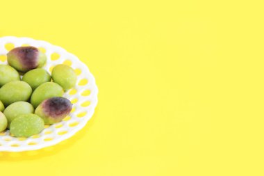 Sarı arka planda dekoratif bir tabakta doğal yeşil ve kahverengi zeytinler.