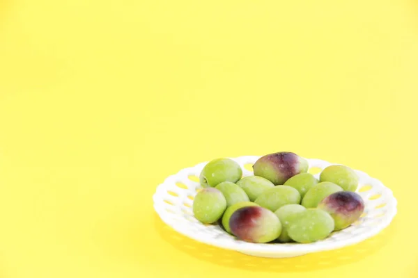Natürliche grüne und braune Oliven in einem dekorativen Teller auf gelbem Hintergrund — Stockfoto