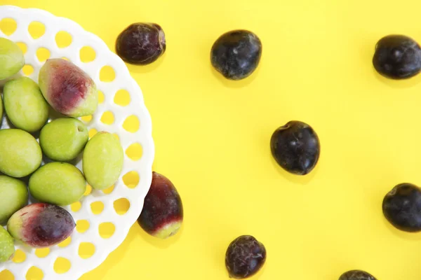 Olives vertes et brunes rondes naturelles dans une assiette décorative sur fond jaune — Photo