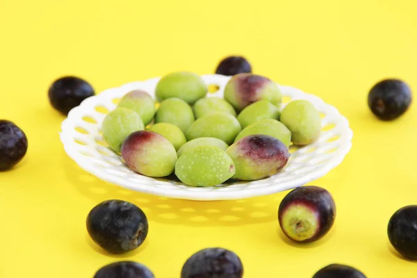 Natürliche runde grüne und braune Oliven in einem dekorativen Teller auf gelbem Hintergrund — Stockfoto