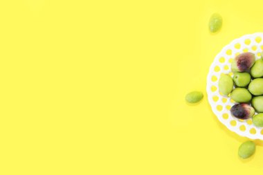 natural fresh green and burgundy olives in a white decorative plate on a yellow background