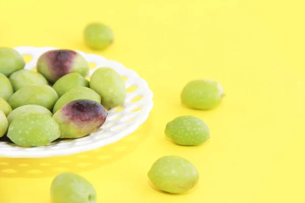 Olives vertes fraîches et bordeaux naturelles dans une assiette décorative blanche sur fond jaune — Photo