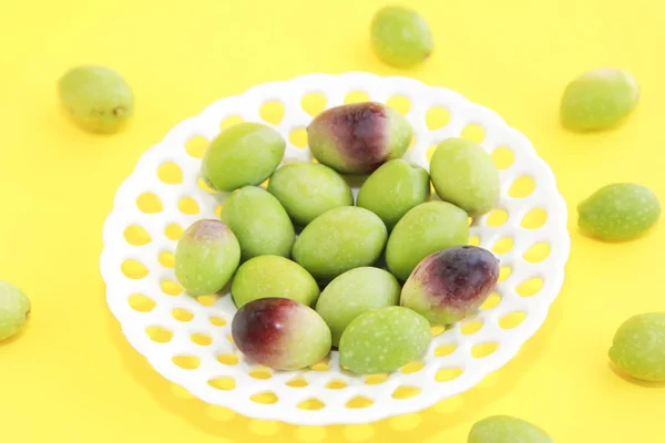 Olives vertes fraîches et bordeaux naturelles dans une assiette décorative blanche sur fond jaune — Photo