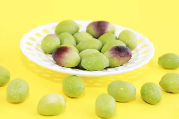 Olives vertes fraîches et bordeaux naturelles dans une assiette décorative blanche sur fond jaune — Photo