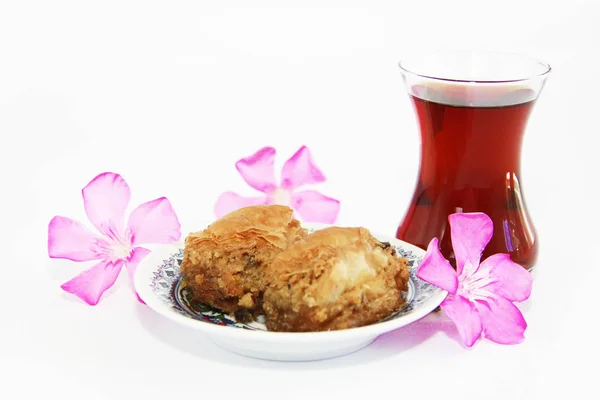 Plato dulce oriental tradicional nacional baklava, té turco en un vaso y flores rosadas — Foto de Stock