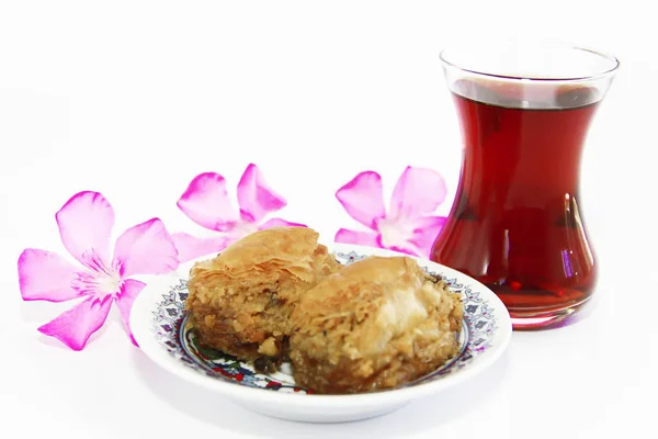 Plato dulce oriental tradicional nacional baklava, té turco en un vaso y flores rosadas — Foto de Stock