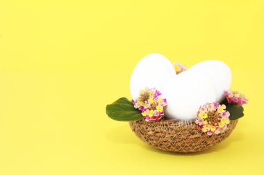 decorative white eggs in a straw basket with pink flowers for easter