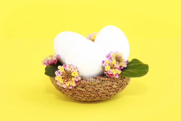 Huevos blancos decorativos en una cesta de paja con flores rosadas para Pascua — Foto de Stock