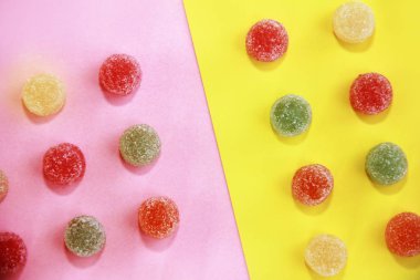 Çok renkli şeker marmelatı, pembe sarı arka planda şeker parçacıkları.