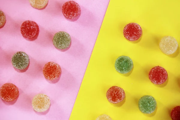 Dulce mermelada de caramelo multicolor en azúcar espolvorea sobre un fondo amarillo rosado — Foto de Stock