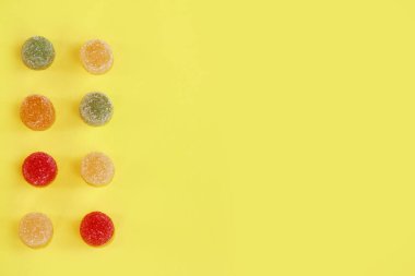 Tatlı, yuvarlak, çok renkli marmelat tatlısı. Sarı arka planda şeker parçacıkları serpiştiriyor.