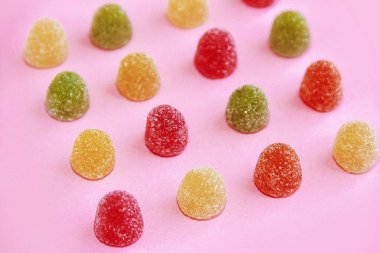 yuvarlak, çok renkli şeker marmeladı pembe bir arka planda şeker parçacıkları serpiştiriyor.