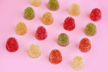 yuvarlak, çok renkli şeker marmeladı pembe bir arka planda şeker parçacıkları serpiştiriyor.