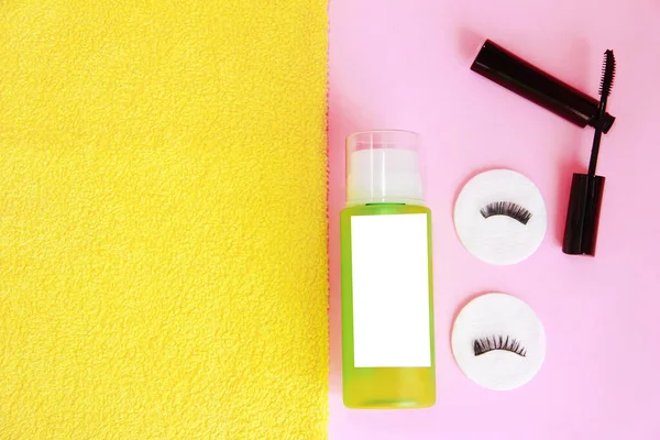 cosmetics, lotion, mascara, cotton pads on yellow and pink background