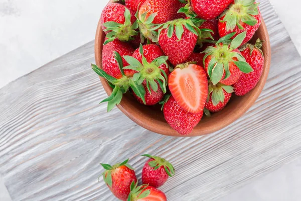 Beyaz ahşap zemin üzerinde bir kapta sulu taze çilek