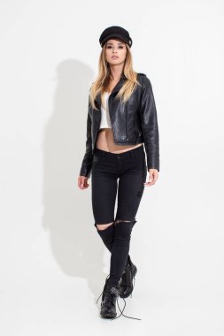 Deri ceketli ve siyah pantolonlu beyaz arka planda poz veren bir kız. Moda çekimi.