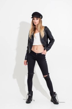 Deri ceketli ve siyah pantolonlu beyaz arka planda poz veren bir kız. Moda çekimi.