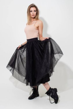 Açık tişörtlü ve siyah etekli güzel bir kız beyaz arka planda poz veriyor. Moda çekimi.