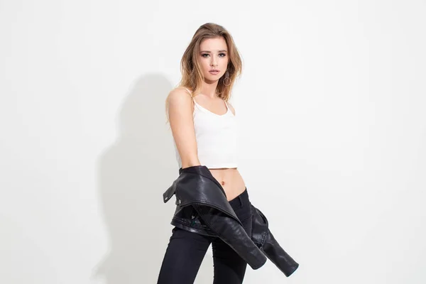 Deri ceketli ve siyah pantolonlu beyaz arka planda poz veren bir kız. Moda çekimi.