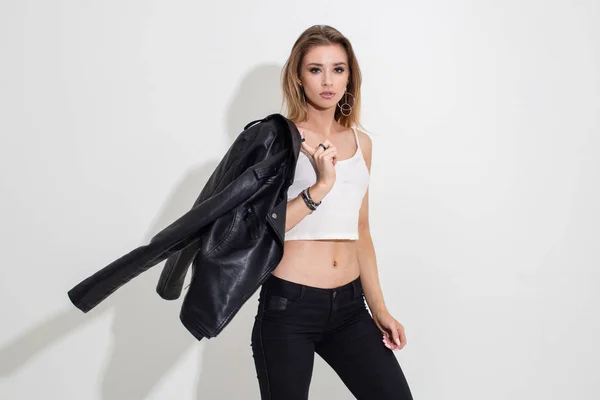 Deri ceketli ve siyah pantolonlu beyaz arka planda poz veren bir kız. Moda çekimi.