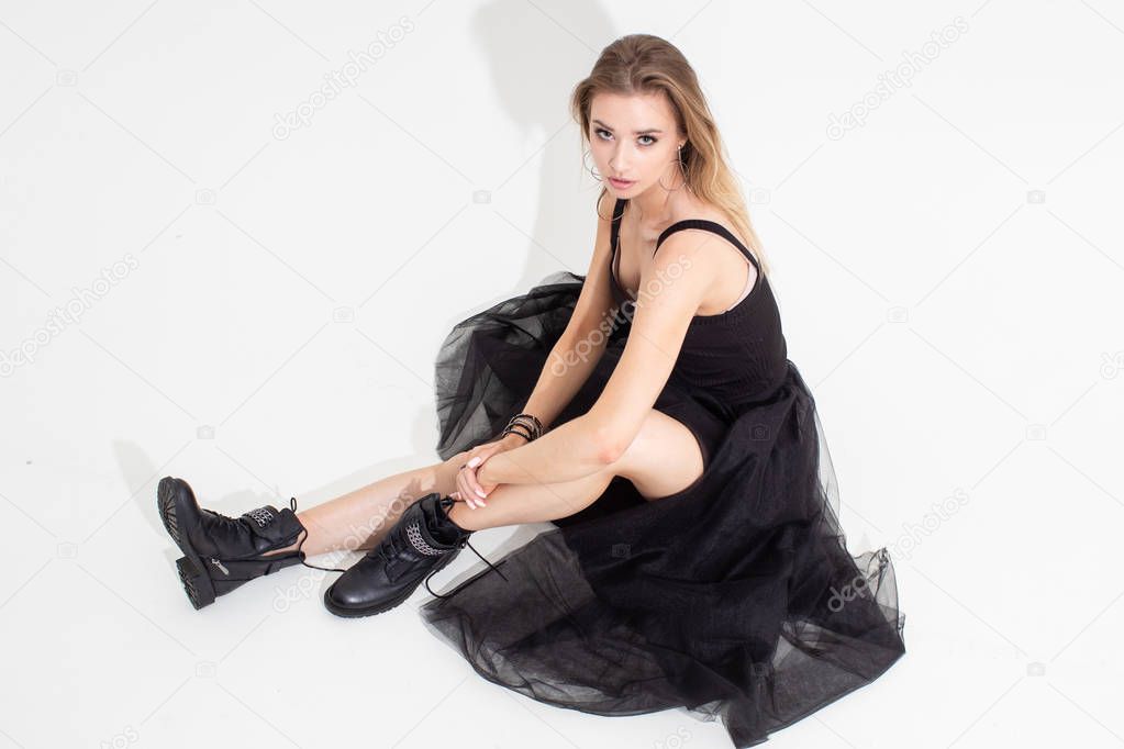A girl in a t-shirt and black skirt sits on the floor on a white background. Fashion shooting