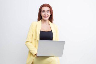 Sarı elbiseli kızıl saçlı bir kız bir sandalyeye oturur ve dizüstü bilgisayarda çalışır.