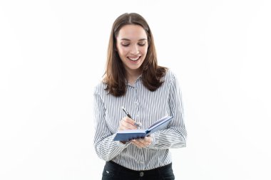 Çizgili tişörtlü bir kız mavi defterine yazıyor.