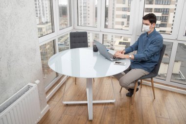 Koruyucu yüz maskeli bir adam virüs salgını sırasında evden bilgisayarın başında çalışıyor. Virüs enfeksiyonu sırasında karantina