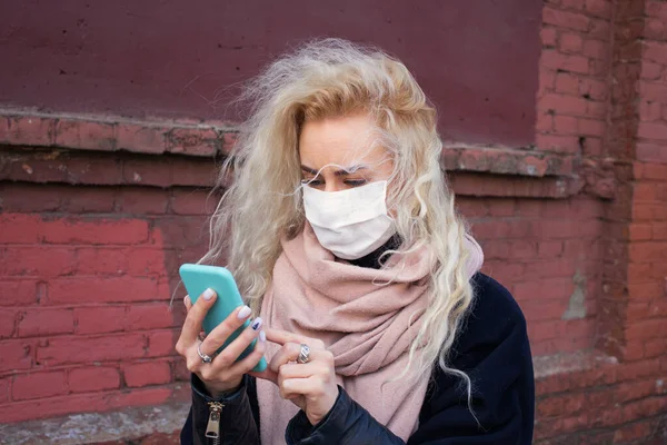 The girl reads the news on the phone and walks around the city in a protective medical mask. Virus epidemic in the world
