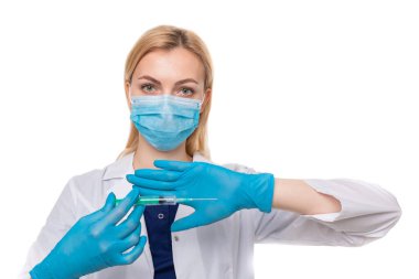 Tıbbi maskeli ve eldivenli bir kız doktor elinde beyaz bir arka planda şırınga tutuyor.