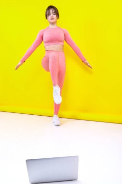 Atletik kız, sarı arka planda dizüstü bilgisayar izleyerek evde antrenman yapıyor.