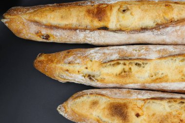 Koyu arkaplanda üç taze Fransız ekmeği.