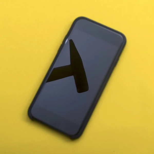 Der Hammer spiegelt sich auf dem Telefonbildschirm auf gelbem Hintergrund. Handyreparaturkonzept — Stockbild Der Hammer Spiegelt Sich Auf Dem Telefonbildschirm Auf Gelbem Hintergrund — Stockfoto