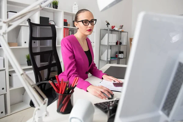 A girl in a business style works at a computer in office