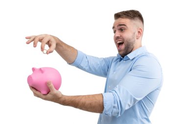 Mavi gömlekli bir adam pembe domuz kumbarasına bozuk para atıyor.