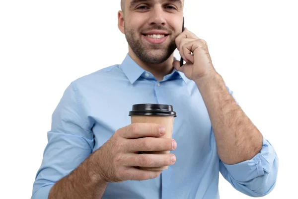 A young guy drinks coffee and talks on the phone. Start of the working day