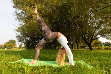 Parkta yoga yapan bir kız ellerinin üzerinde duruyor.