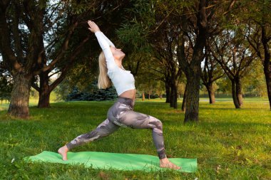 Sportif sarışın parkta yoga yapıyor.