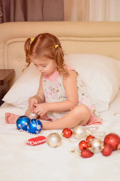 Menina em casa na cama brincando com bolas de Natal. No Natal. Feriados — Fotografia de Stock