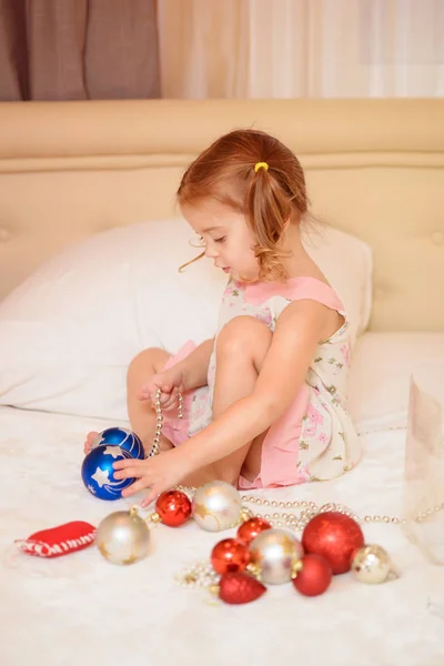 Petite fille à la maison au lit jouant avec des boules de Noël. Noël. Vacances — Photo