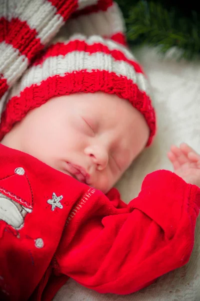 Μωρό σε ένα κόκκινο κοστούμι Σάντα σε ένα Χριστουγεννιάτικο στεφάνι από βελόνες πεύκων με εορταστική διακόσμηση — Φωτογραφία Αρχείου